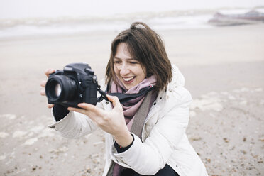 Porträt einer entspannten Frau, die am Strand Fotos mit einer Kamera macht - KMKF00749