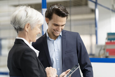 Lächelnder Geschäftsmann und ältere Geschäftsfrau mit Tablet im Gespräch in einer Fabrik - DIGF05636