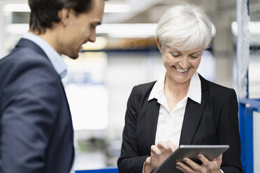 Lächelnder Geschäftsmann und ältere Geschäftsfrau mit Tablet im Gespräch in einer Fabrik - DIGF05637