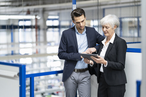 Geschäftsmann und ältere Geschäftsfrau mit Tablet im Gespräch in einer Fabrik - DIGF05639