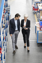 Businessman and senior businesswoman with tablet walking in a factory - DIGF05646