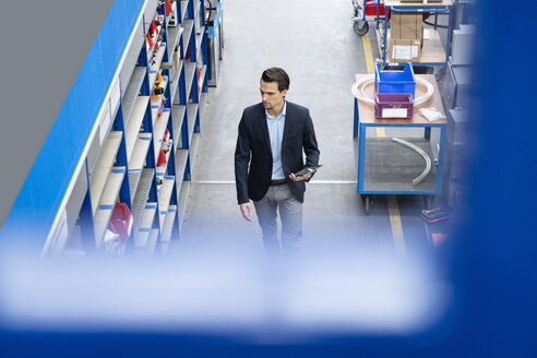 Businessman with tablet walking in a factory - DIGF05651