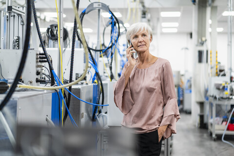 Ältere Frau telefoniert mit Handy in einer Fabrik, lizenzfreies Stockfoto