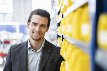 Portrait of smiling businessman in storehouse of a factory - DIGF05673