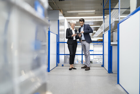 Geschäftsmann und ältere Geschäftsfrau mit Tablet im Gespräch in einer Fabrik, lizenzfreies Stockfoto