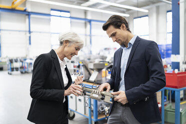Businessman and senior businesswoman examining workpiece in a factory - DIGF05702