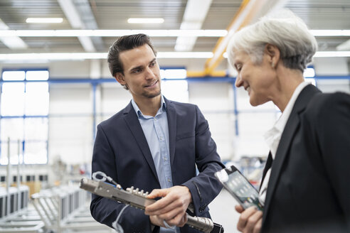 Ein lächelnder Geschäftsmann und eine ältere Geschäftsfrau begutachten ein Werkstück in einer Fabrik - DIGF05705