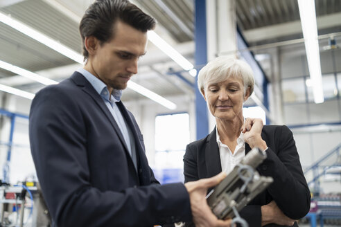 Geschäftsmann und ältere Geschäftsfrau prüfen ein Werkstück in einer Fabrik - DIGF05708