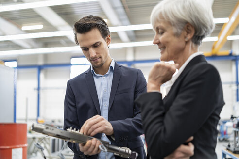 Ein lächelnder Geschäftsmann und eine ältere Geschäftsfrau begutachten ein Werkstück in einer Fabrik - DIGF05709