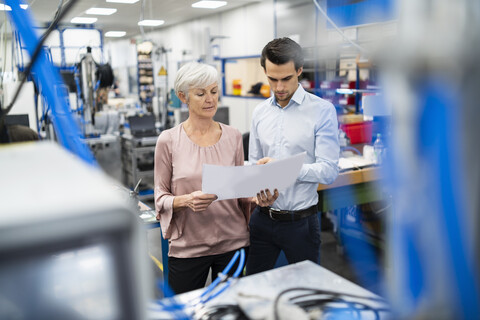 Geschäftsmann und ältere Frau betrachten einen Plan in einer Fabrik, lizenzfreies Stockfoto