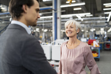 Smiling senior businesswoman and businessman talking in a factory - DIGF05720