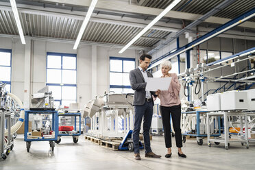 Businessman and senior woman looking at plan in a factory - DIGF05722