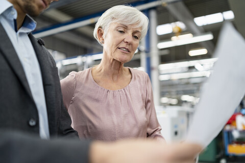 Businessman and senior woman looking at plan in a factory stock photo