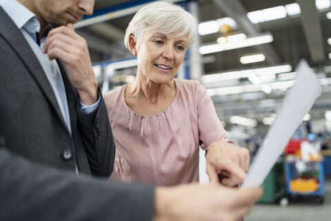 Geschäftsmann und ältere Frau betrachten einen Plan in einer Fabrik, lizenzfreies Stockfoto