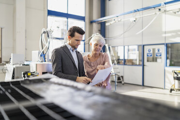 Businessman and senior woman looking at plan in a factory - DIGF05728