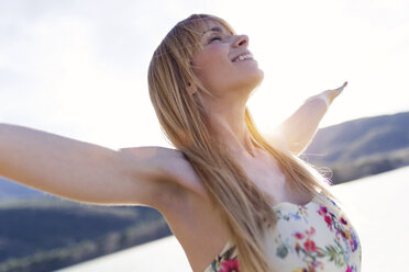 Happy blond woman in front of lake - JSRF00107