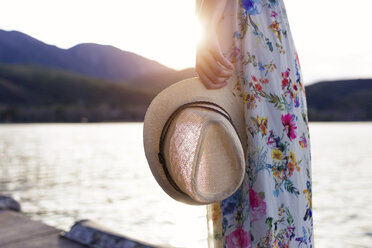 Junge Frau im Sommerkleid mit Blumenmuster steht auf einem Steg und hält einen Sommerhut, Teilansicht - JSRF00108