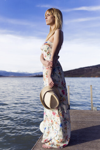 Spanien, Cellers, nachdenkliche junge Frau im Sommerkleid mit Blumenmuster auf dem Steg stehend, lizenzfreies Stockfoto