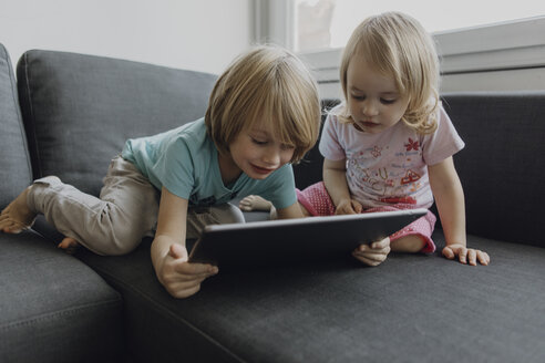 Bruder und kleine Schwester benutzen ein digitales Tablet auf der Couch zu Hause - JLOF00303