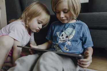 Bruder und kleine Schwester sitzen zu Hause auf dem Boden und benutzen ein digitales Tablet - JLOF00306