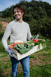 Mann trägt Kiste mit frisch geerntetem Gemüse aus seinem Gemüsegarten - GEMF02697