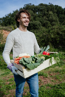 Mann trägt Kiste mit frisch geerntetem Gemüse aus seinem Gemüsegarten - GEMF02698