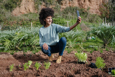 Woman taking selfies of planting lettuce seedlings in an vegetable garden - GEMF02701