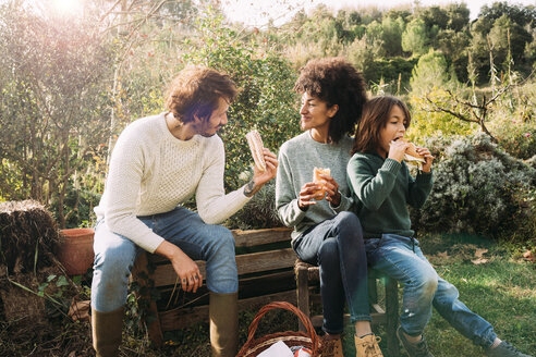 Glückliche Familie, die im Garten sitzt, eine Pause macht und Sandwiches isst - GEMF02714