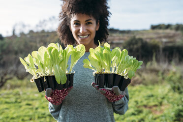 Smiling woman holding lettuce seedlings in a vegetable garden - GEMF02726