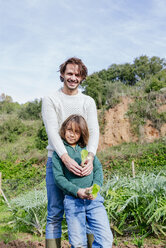 Father and son holding lettuce seedlings in a vegetable garden - GEMF02763