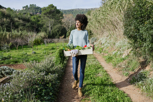 Frau geht auf dem Feld und trägt eine Gemüsekiste - GEMF02787