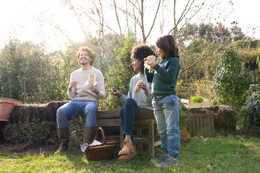 Glückliche Familie sitzt im Garten, macht eine Pause und isst Sandwiches - GEMF02796