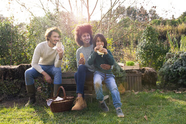 Glückliche Familie sitzt im Garten, macht eine Pause und isst Sandwiches - GEMF02797