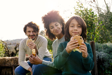 Happy family sitting in garden, taking a break, eating sandwiches - GEMF02798