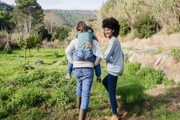 Happy family walking in the countryside, father carrying son piggyback - GEMF02810