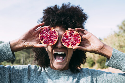 Frau auf dem Lande, die Augen mit halbierten Granatäpfeln bedeckt, lizenzfreies Stockfoto