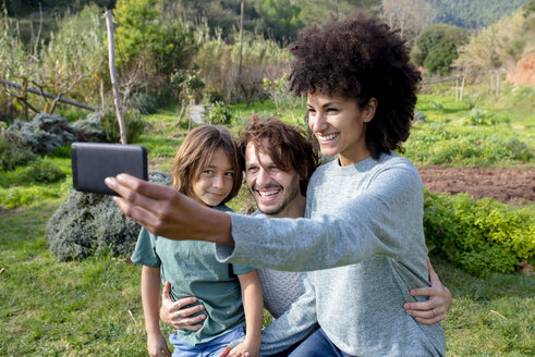 Glückliche Familie sitzt auf einer Bank im Garten, Mutter macht Selfies - GEMF02839