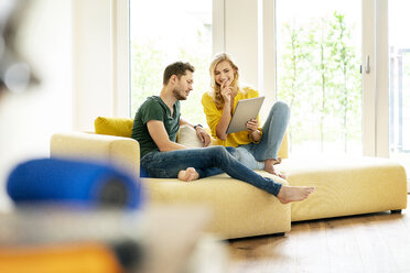 Couple sitting on couch in their new home, using digital tablet - PESF01426