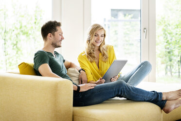 Couple sitting on couch in their new home, using digital tablet - PESF01427