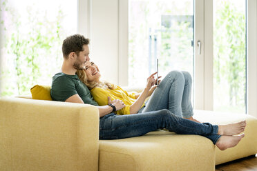 Couple sitting on couch in their new home, using digital tablet - PESF01428