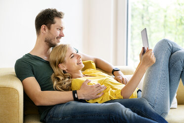 Couple sitting on couch in their new home, using digital tablet - PESF01430