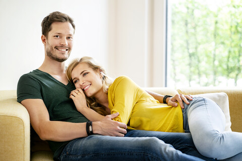 Ehepaar sitzt auf der Couch in ihrem neuen Zuhause und kuschelt, lizenzfreies Stockfoto