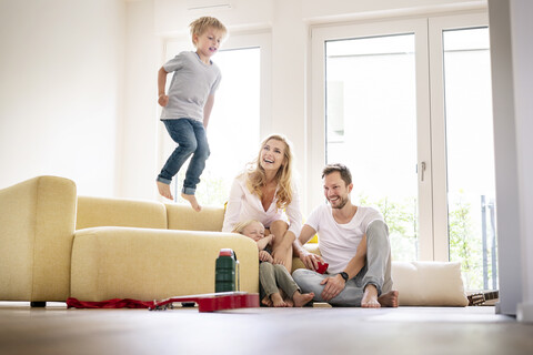 Glückliche Familie beim Einzug in ihr neues Haus, Junge springt auf der Couch herum, lizenzfreies Stockfoto