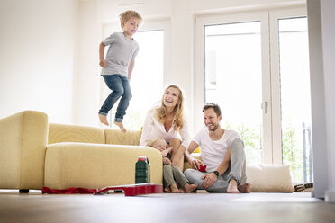 Happy family moving into their new home, boy jumping on couch - PESF01444