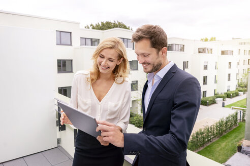 Real estate agent standing on a balcony with customer, looking at digital tablet - PESF01462