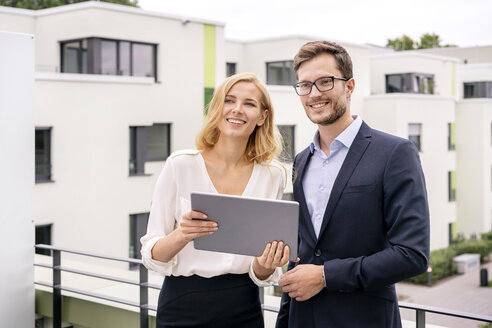 Real estate agent standing on a balcony with customer, looking at digital tablet - PESF01466