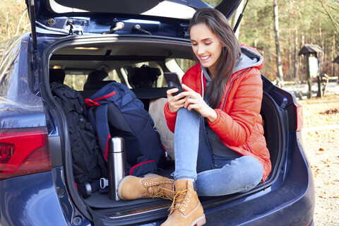 Frau benutzt Smartphone im Kofferraum während einer Autofahrt, lizenzfreies Stockfoto