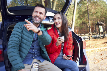 Couple pointing and looking away while sitting in car trunk during road trip - BSZF00904