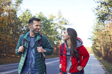 Happy couple walking along road in the woods during backpacking trip - BSZF00905