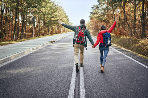 Glückliches Paar, das mitten auf einer leeren Straße im Wald spazieren geht, lizenzfreies Stockfoto